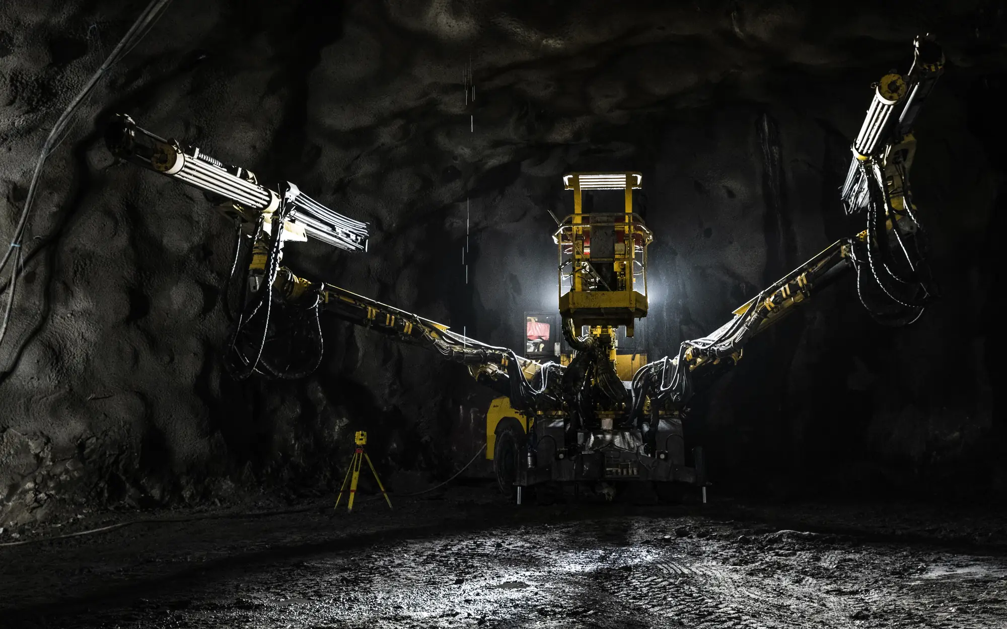 A drill jumbo parked at the face of an underground heading, its booms extended