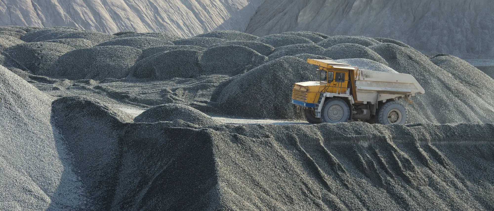 A haul truck threading between grey crushed-stone stockpiles at a quarry
